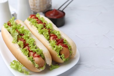 Tasty hot dogs with lettuce and ketchup on white table, closeup. Space for text