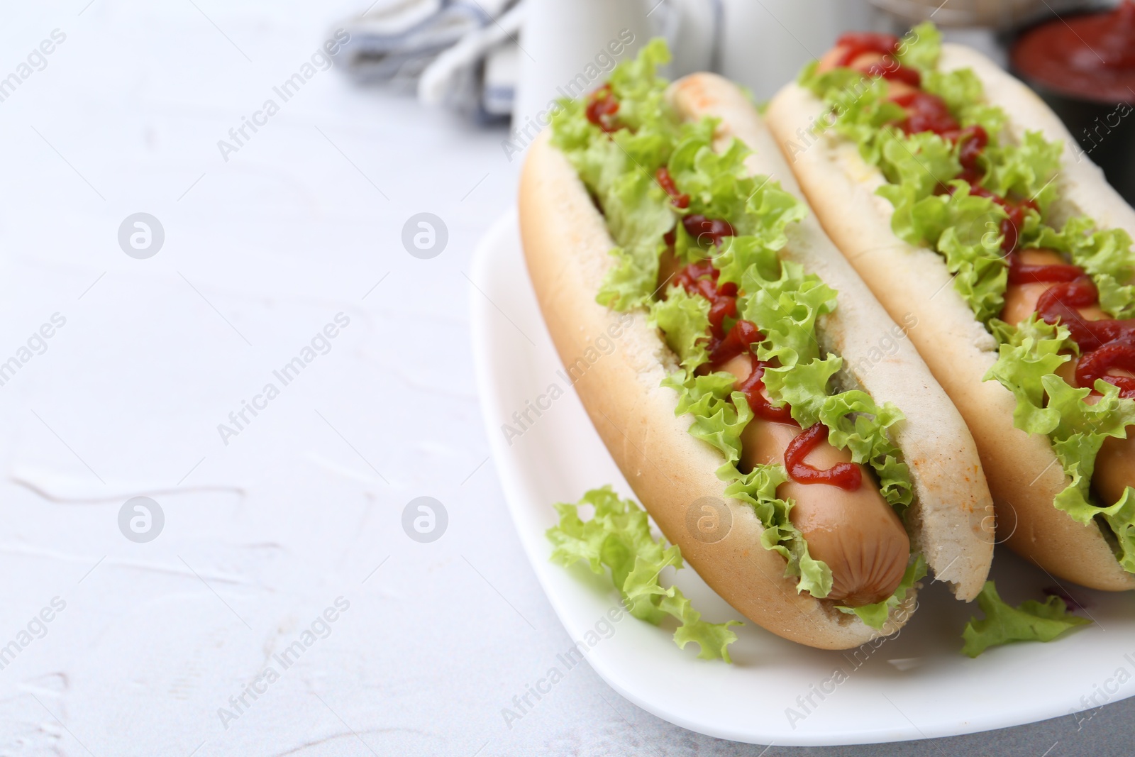 Photo of Tasty hot dogs with lettuce and ketchup on white table, closeup. Space for text