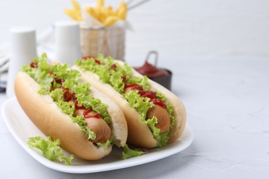 Photo of Tasty hot dogs with lettuce and ketchup on white table, closeup. Space for text