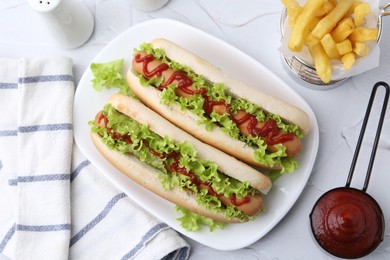 Photo of Tasty hot dogs with lettuce, ketchup and potato fries on white table, flat lay