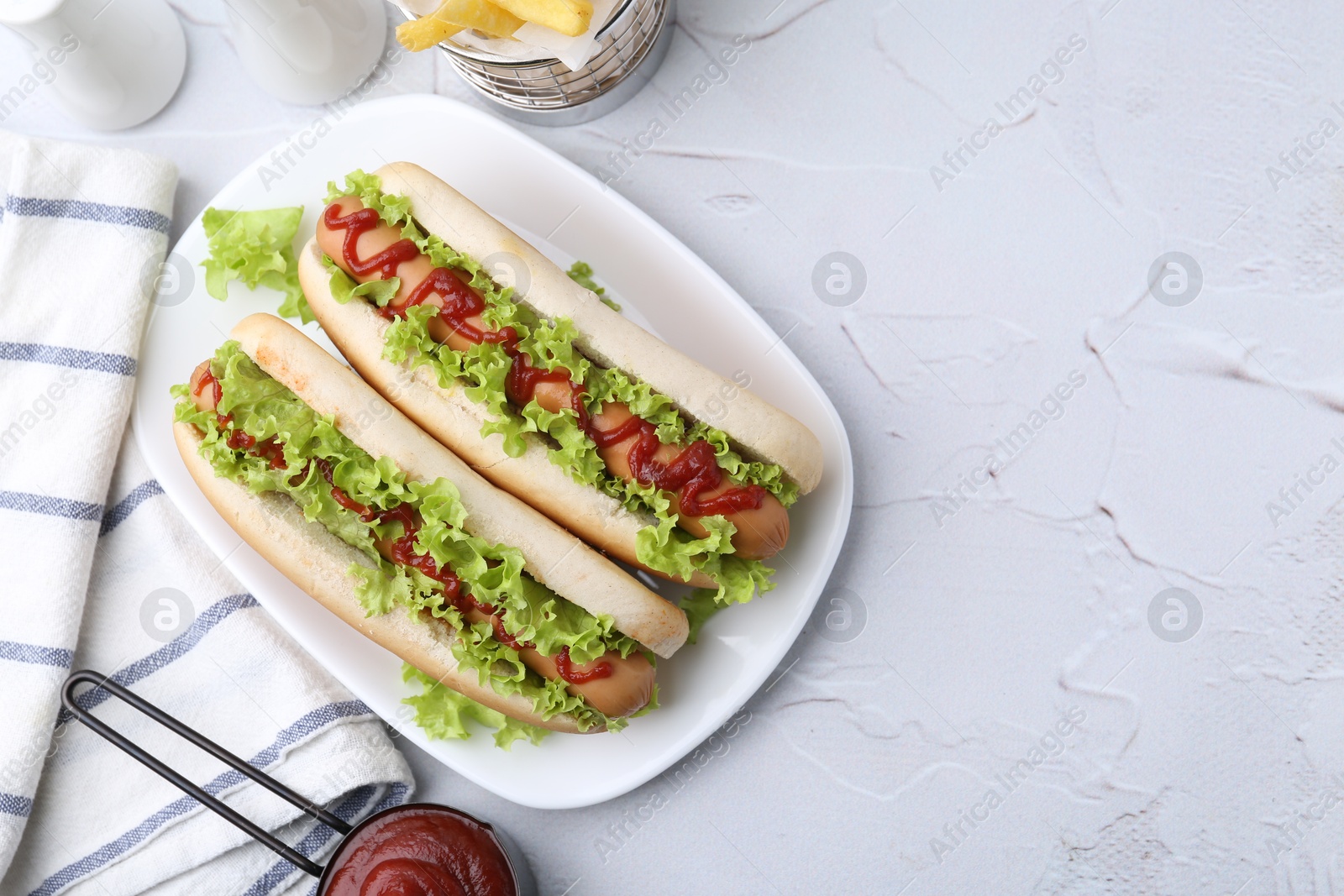 Photo of Tasty hot dogs with lettuce and ketchup on white table, flat lay. Space for text