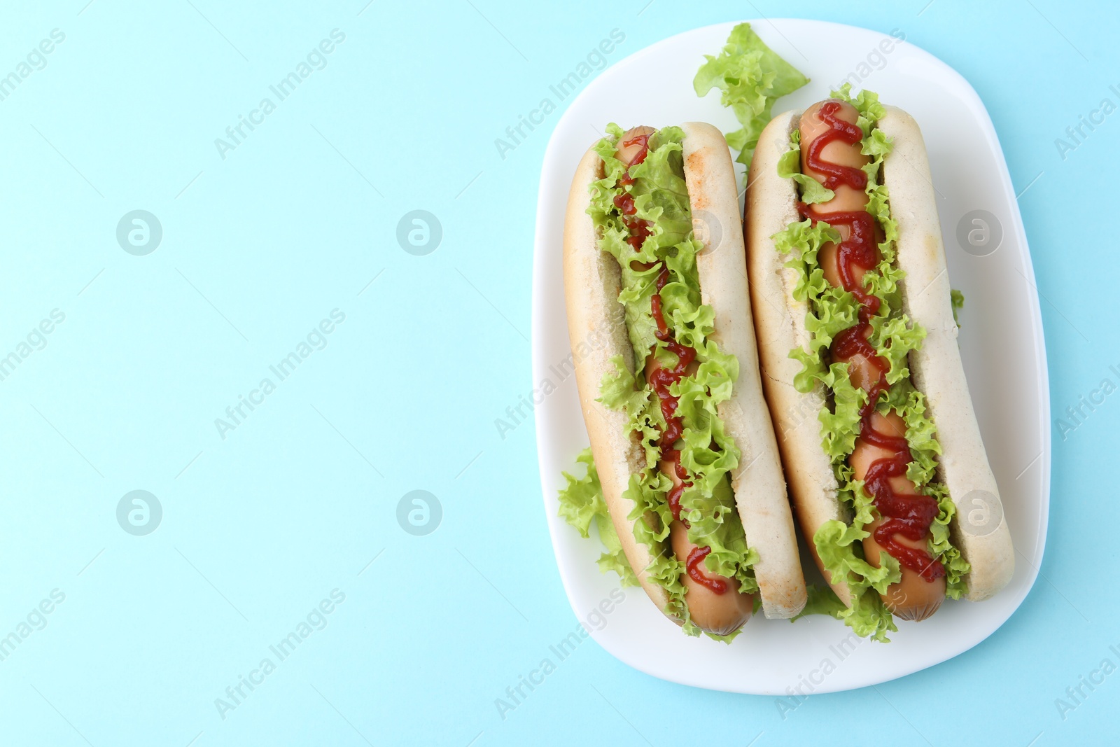 Photo of Tasty hot dogs with lettuce and ketchup on light blue background, top view. Space for text