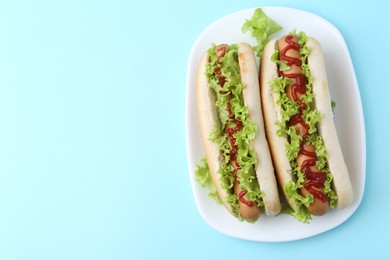 Photo of Tasty hot dogs with lettuce and ketchup on light blue background, top view. Space for text