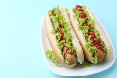 Tasty hot dogs with lettuce and ketchup on light blue background, closeup. Space for text