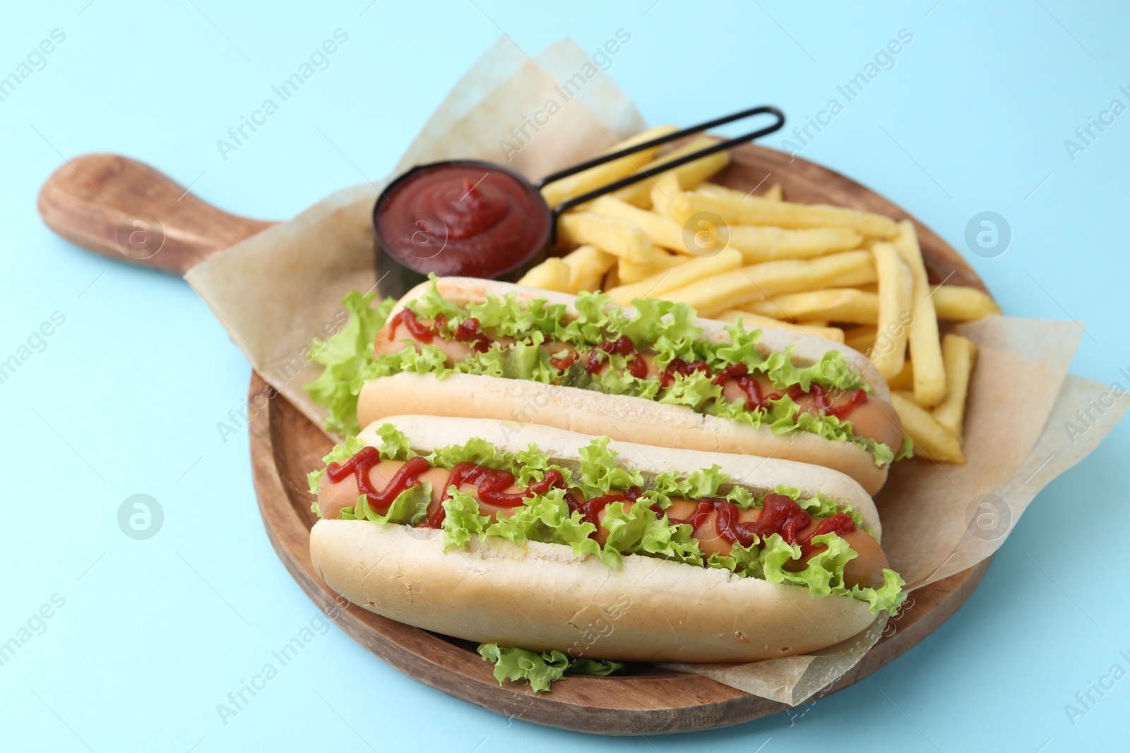 Photo of Tasty hot dogs with lettuce, ketchup and potato fries on light blue background, closeup