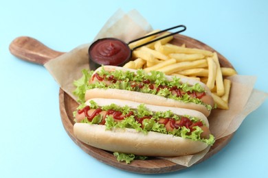 Tasty hot dogs with lettuce, ketchup and potato fries on light blue background, closeup