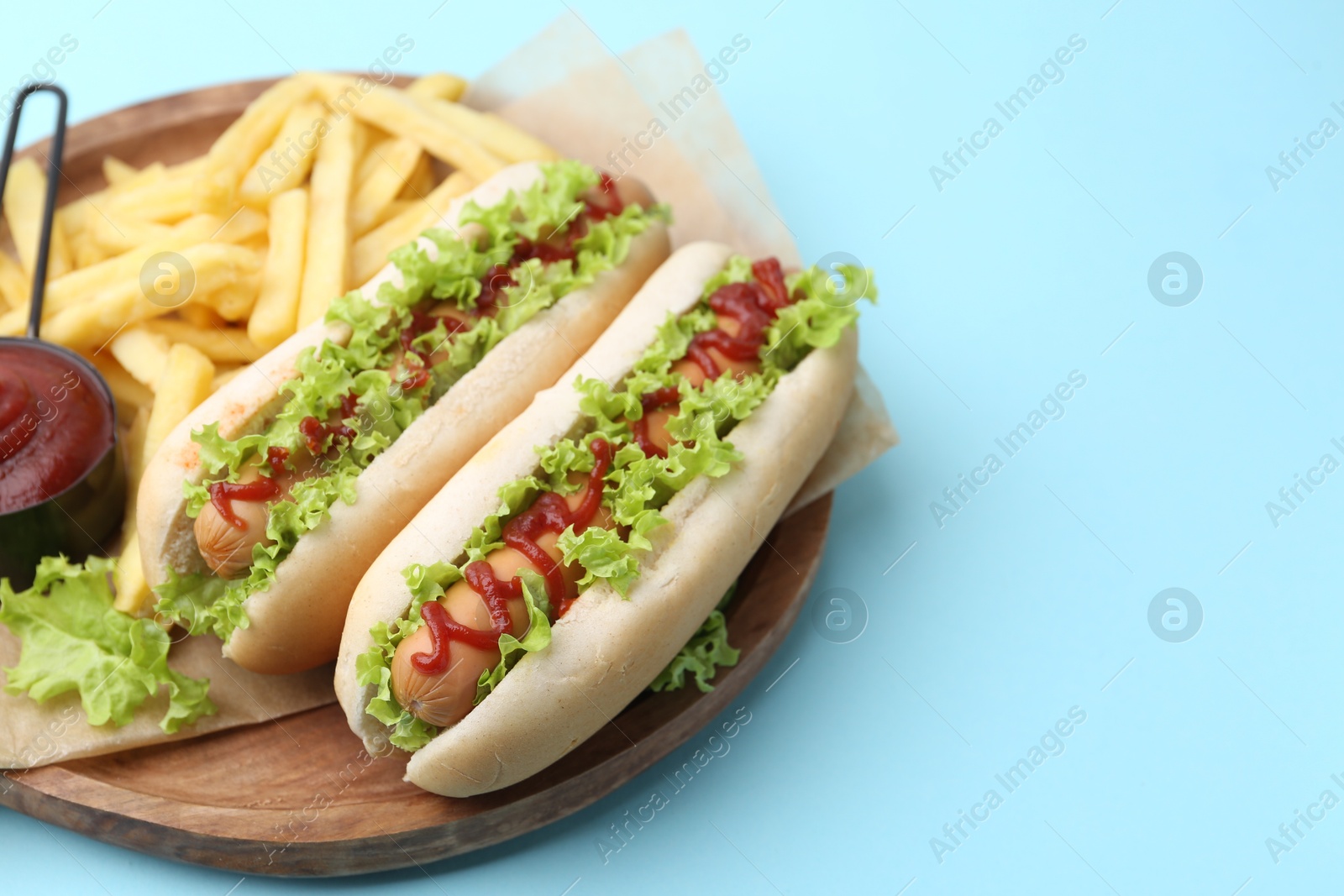 Photo of Tasty hot dogs with lettuce, ketchup and potato fries on light blue background, closeup. Space for text