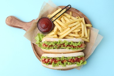 Tasty hot dogs with lettuce, ketchup and potato fries on light blue background, top view