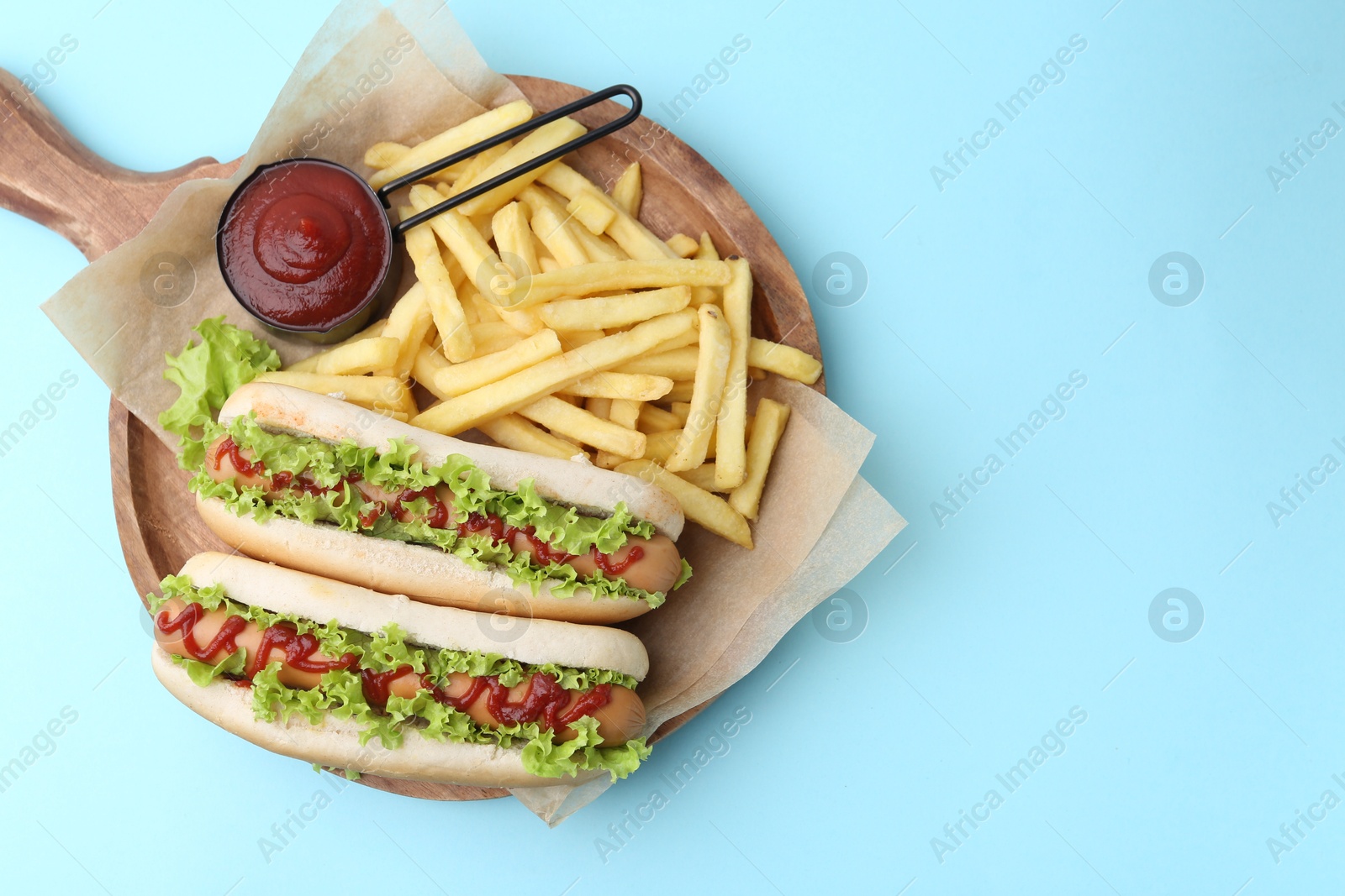 Photo of Tasty hot dogs with lettuce, ketchup and potato fries on light blue background, top view. Space for text