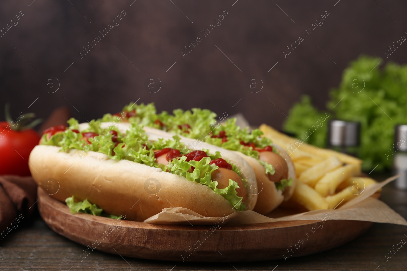 Photo of Tasty hot dogs with lettuce, ketchup and potato fries on wooden table, closeup