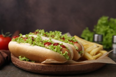 Photo of Tasty hot dogs with lettuce, ketchup and potato fries on wooden table, closeup