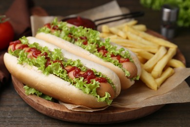 Photo of Tasty hot dogs with lettuce, ketchup and potato fries on wooden table, closeup