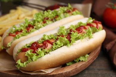 Photo of Tasty hot dogs with lettuce, ketchup and potato fries on wooden table, closeup