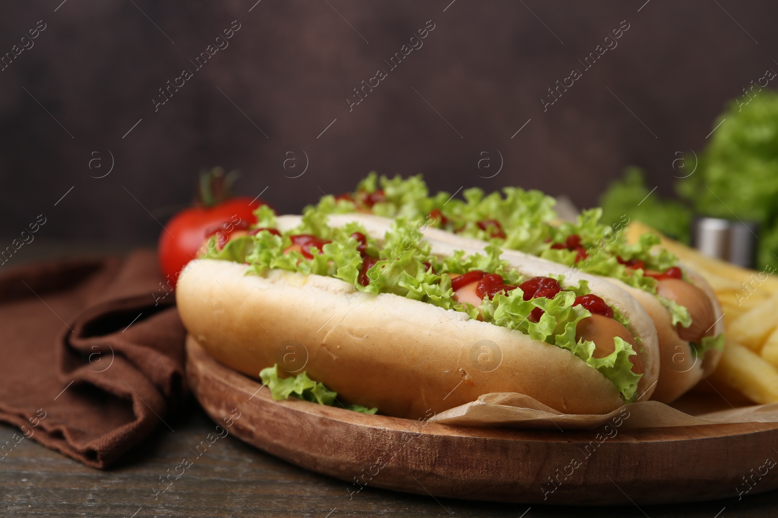 Photo of Tasty hot dogs with lettuce, ketchup and potato fries on wooden table, closeup