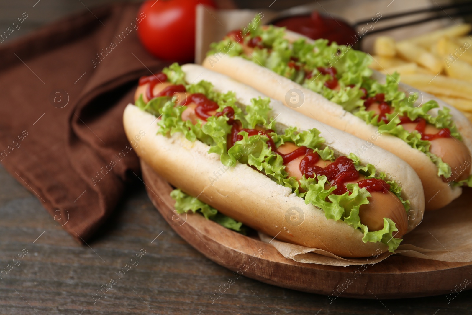 Photo of Tasty hot dogs with lettuce, ketchup and potato fries on wooden table, closeup