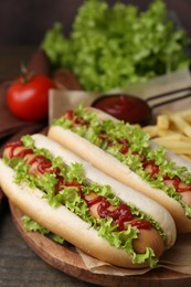 Photo of Tasty hot dogs with lettuce, ketchup and potato fries on wooden table, closeup