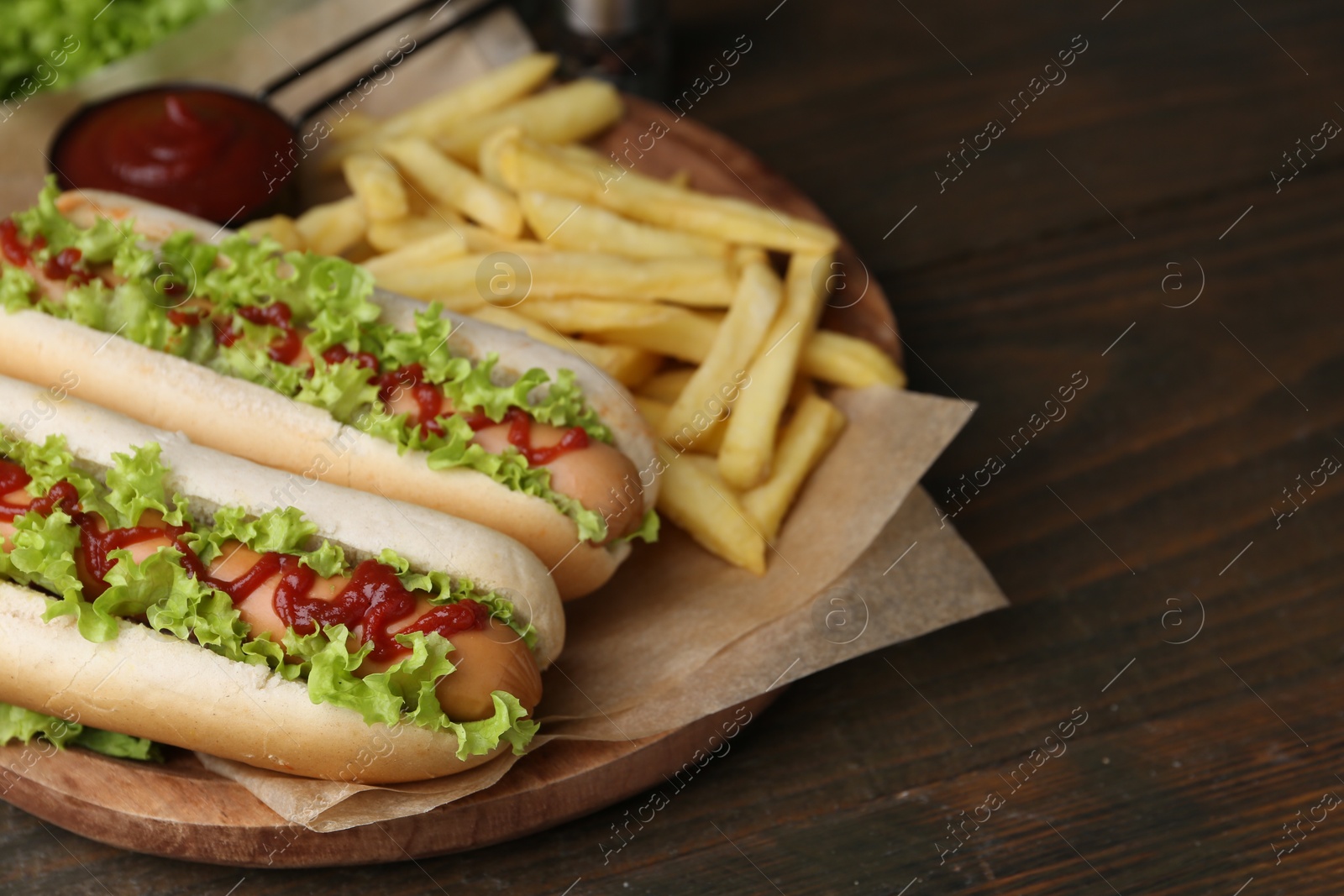 Photo of Tasty hot dogs with lettuce, ketchup and potato fries on wooden table, closeup. Space for text