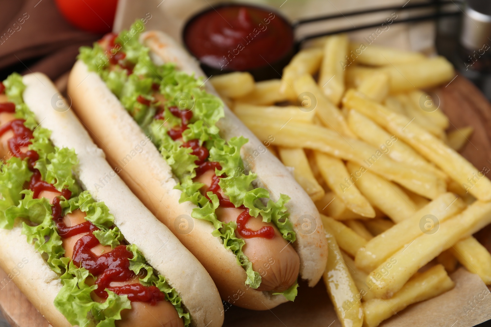 Photo of Tasty hot dogs with lettuce, ketchup and potato fries on wooden table, closeup