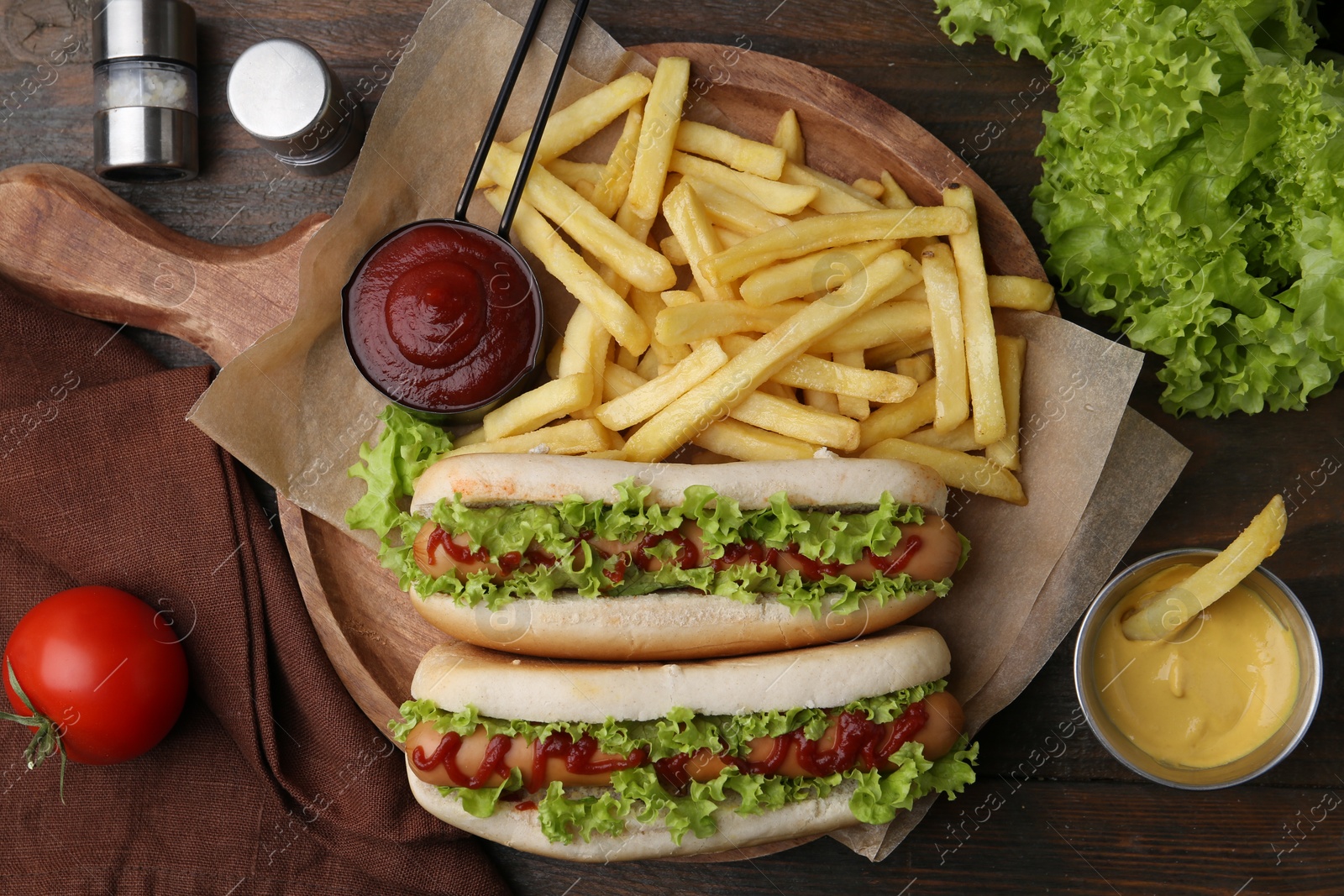 Photo of Tasty hot dogs with lettuce, ketchup and potato fries on wooden table, flat lay