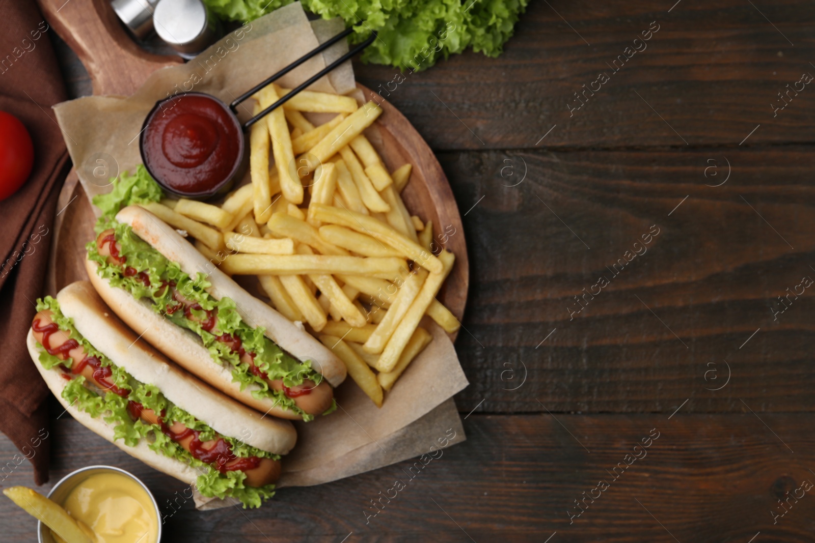 Photo of Tasty hot dogs with lettuce, ketchup and potato fries on wooden table, flat lay. Space for text