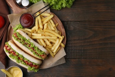 Photo of Tasty hot dogs with lettuce, ketchup and potato fries on wooden table, flat lay. Space for text