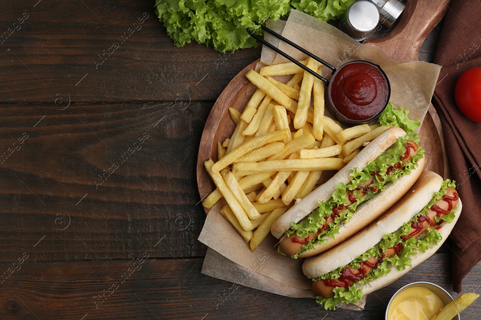 Photo of Tasty hot dogs with lettuce, ketchup and potato fries on wooden table, flat lay. Space for text