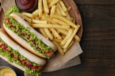 Photo of Tasty hot dogs with lettuce, ketchup and potato fries on wooden table, top view