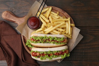 Photo of Tasty hot dogs with lettuce, ketchup and potato fries on wooden table, top view