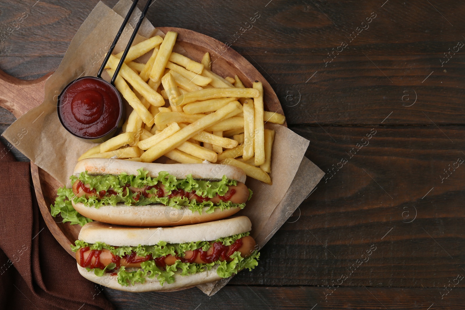 Photo of Tasty hot dogs with lettuce, ketchup and potato fries on wooden table, top view. Space for text