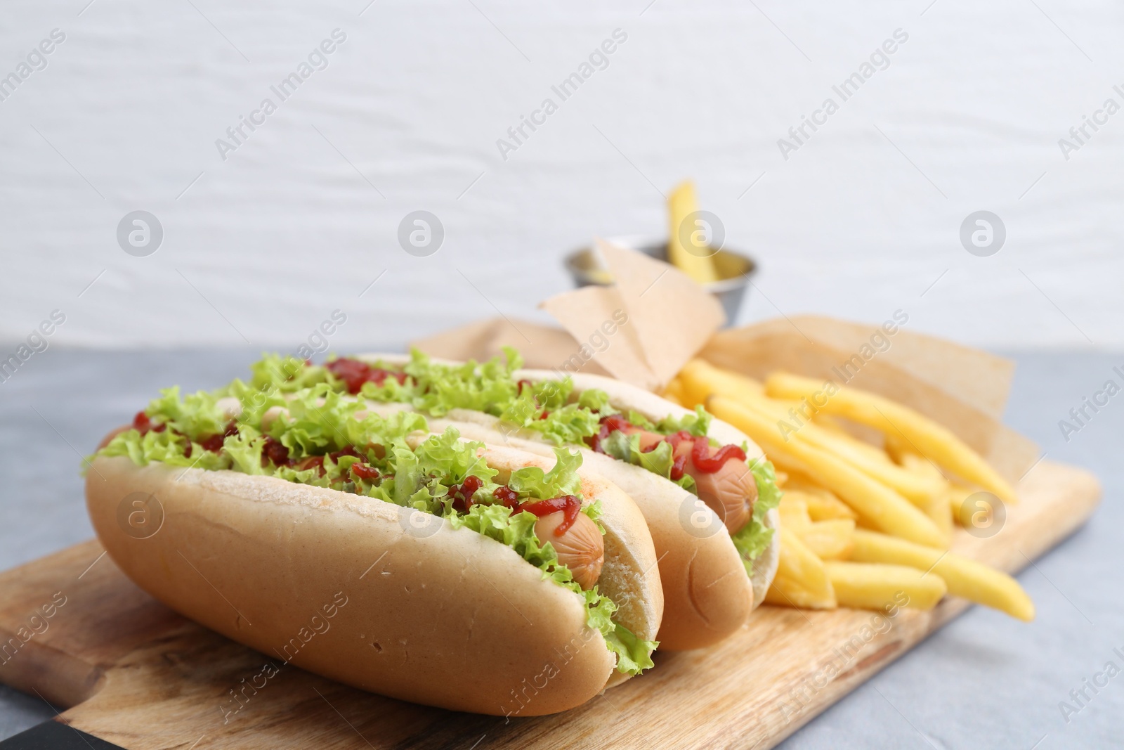 Photo of Tasty hot dogs with lettuce, ketchup and potato fries on light grey table, closeup