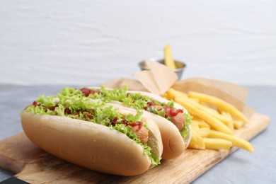 Tasty hot dogs with lettuce, ketchup and potato fries on light grey table, closeup