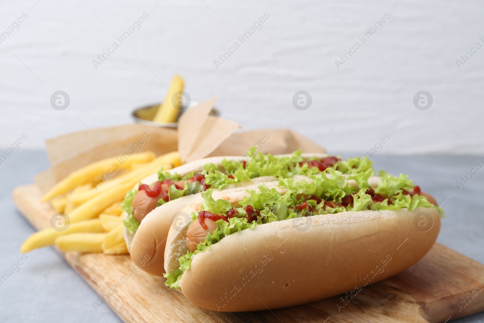 Photo of Tasty hot dogs with lettuce, ketchup and potato fries on light grey table, closeup