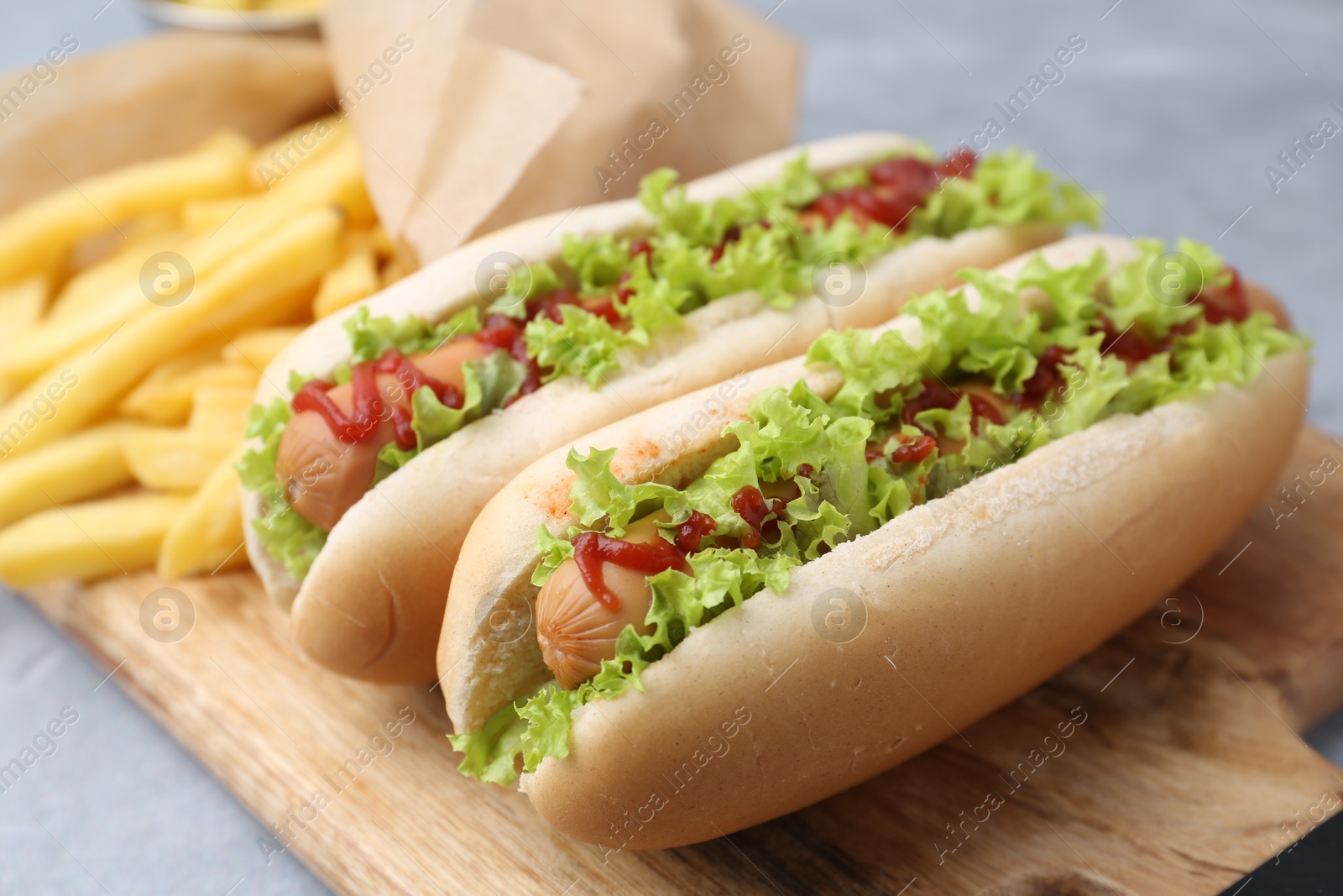 Photo of Tasty hot dogs with lettuce, ketchup and potato fries on light grey table, closeup