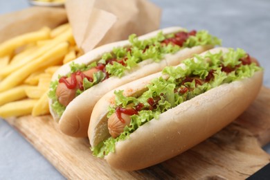 Tasty hot dogs with lettuce, ketchup and potato fries on light grey table, closeup