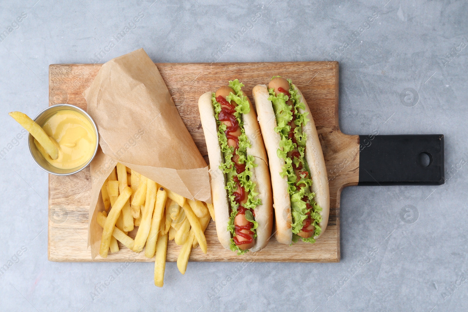 Photo of Tasty hot dogs with lettuce, ketchup and potato fries on light grey table, top view