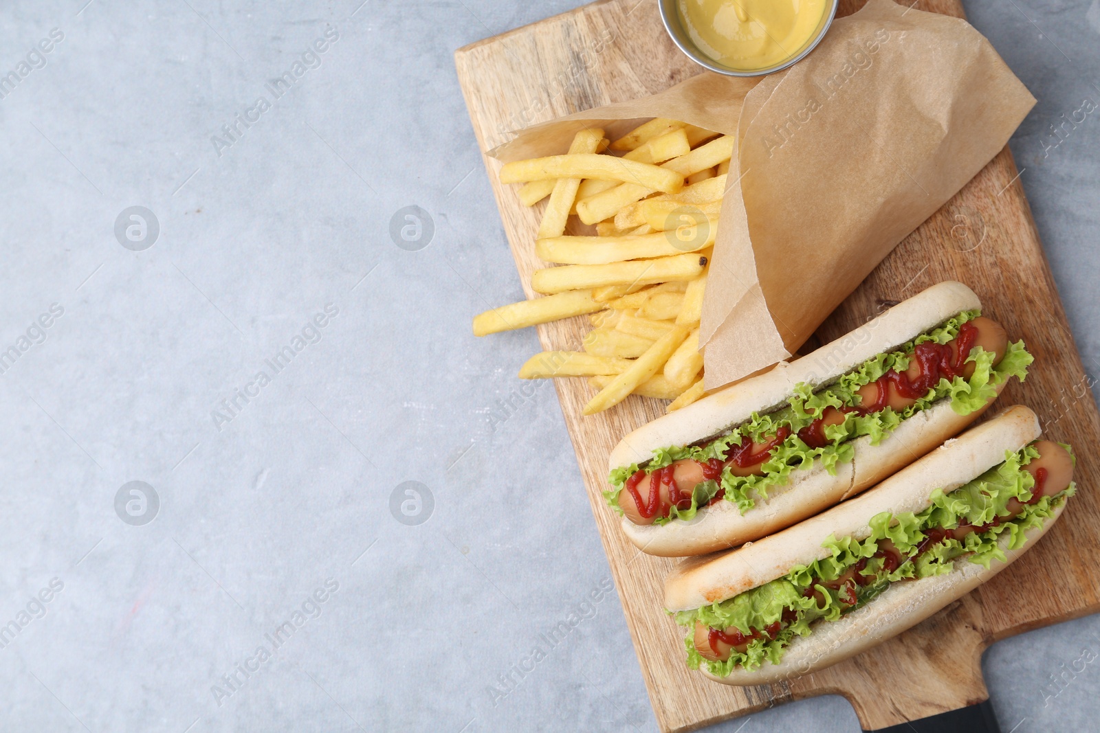 Photo of Tasty hot dogs with lettuce, ketchup and potato fries on light grey table, top view. Space for text