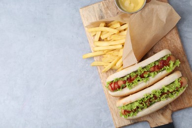 Photo of Tasty hot dogs with lettuce, ketchup and potato fries on light grey table, top view. Space for text