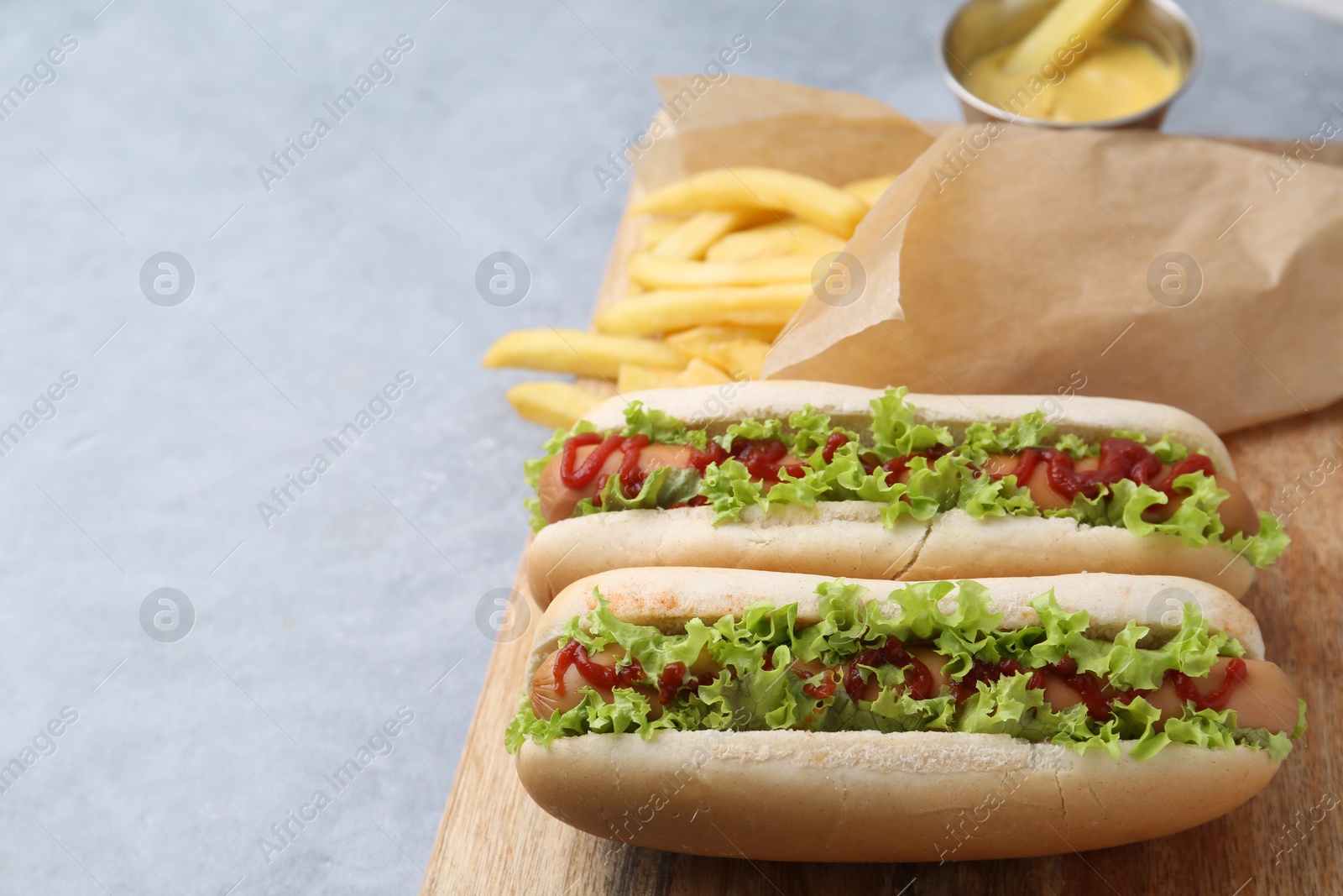 Photo of Tasty hot dogs with lettuce, ketchup and potato fries on light grey table, closeup. Space for text