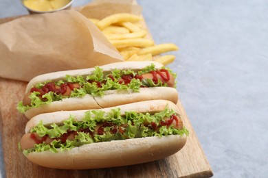 Photo of Tasty hot dogs with lettuce, ketchup and potato fries on light grey table, closeup. Space for text