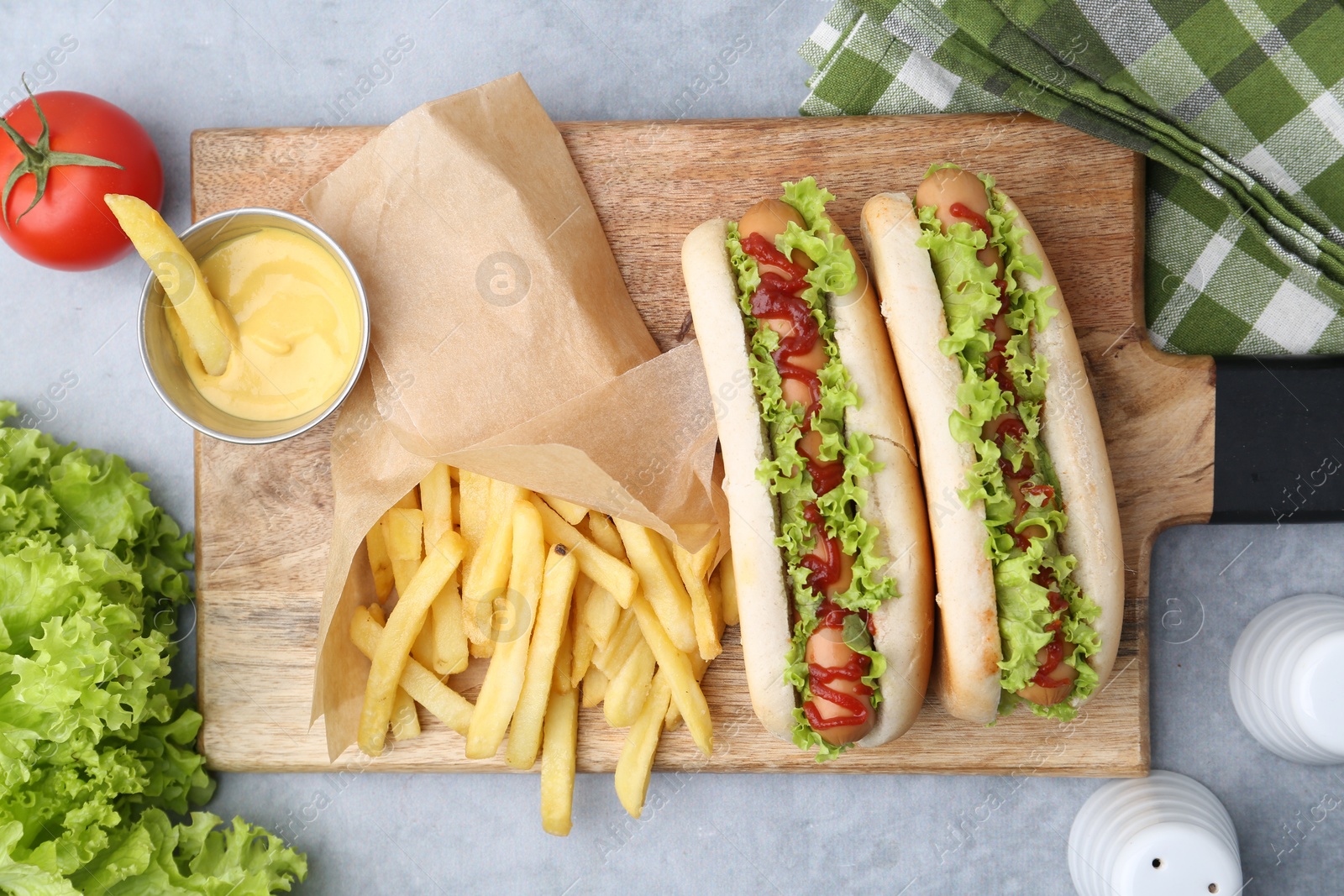 Photo of Tasty hot dogs with lettuce, ketchup and potato fries on light grey table, flat lay