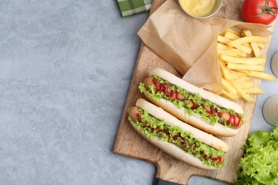 Photo of Tasty hot dogs with lettuce, ketchup and potato fries on light grey table, flat lay. Space for text