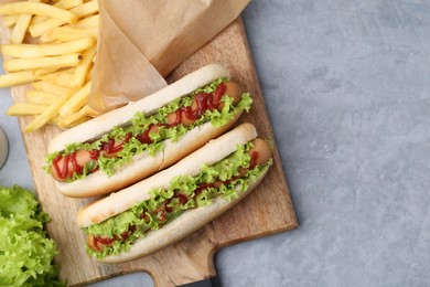 Photo of Tasty hot dogs with lettuce, ketchup and potato fries on light grey table, flat lay. Space for text