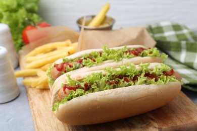 Photo of Tasty hot dogs with lettuce, ketchup and potato fries on light grey table, closeup