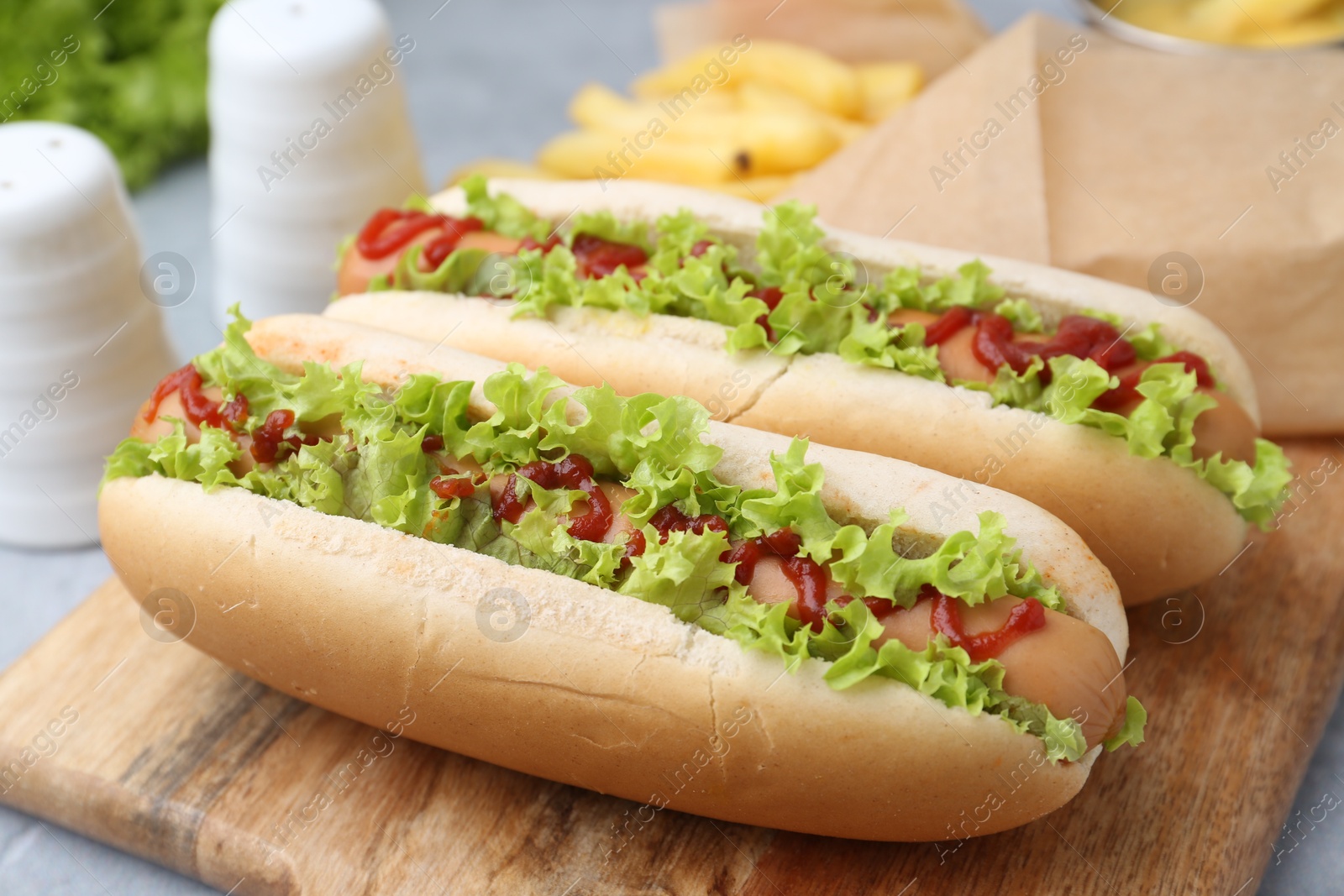 Photo of Tasty hot dogs with lettuce, ketchup and potato fries on light grey table, closeup