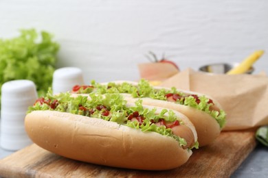 Photo of Tasty hot dogs with lettuce, ketchup and potato fries on light grey table, closeup