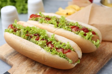 Photo of Tasty hot dogs with lettuce, ketchup and potato fries on light grey table, closeup