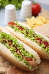 Photo of Tasty hot dogs with lettuce, ketchup and potato fries on table, closeup