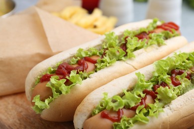 Photo of Tasty hot dogs with lettuce, ketchup and potato fries on table, closeup