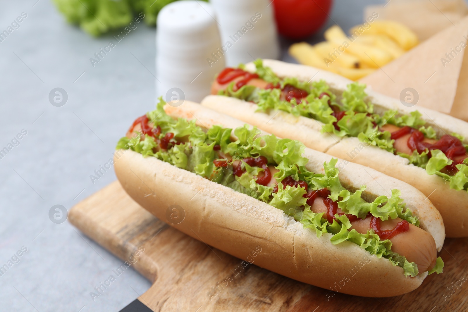 Photo of Tasty hot dogs with lettuce, ketchup and potato fries on light grey table, closeup