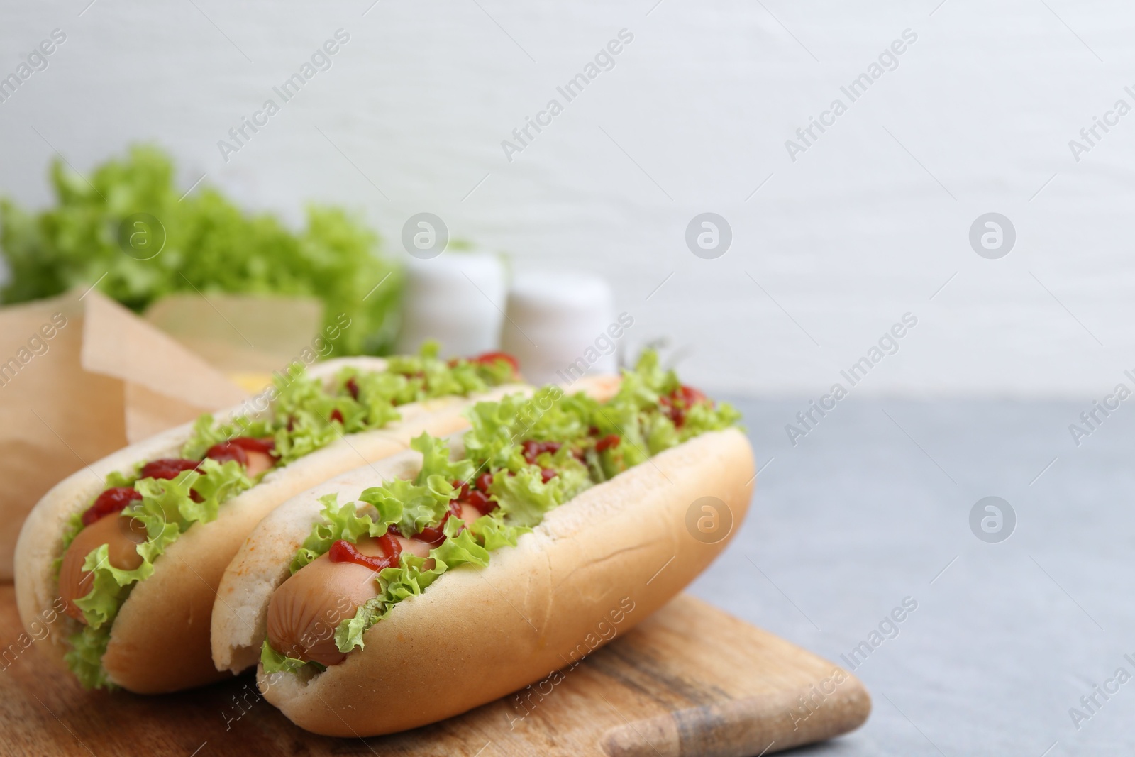 Photo of Tasty hot dogs with lettuce and ketchup on light grey table, closeup. Space for text